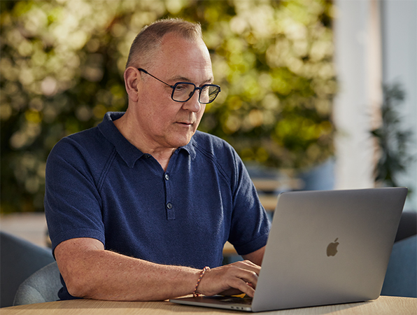 Un empleado de Apple especializado en software y servicios trabaja en un MacBook al aire libre con vegetación de fondo.