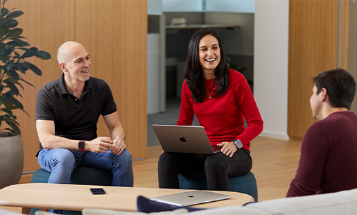 Camila 笑著坐在另外兩位 Apple 員工之間，腿上有一部 MacBook。