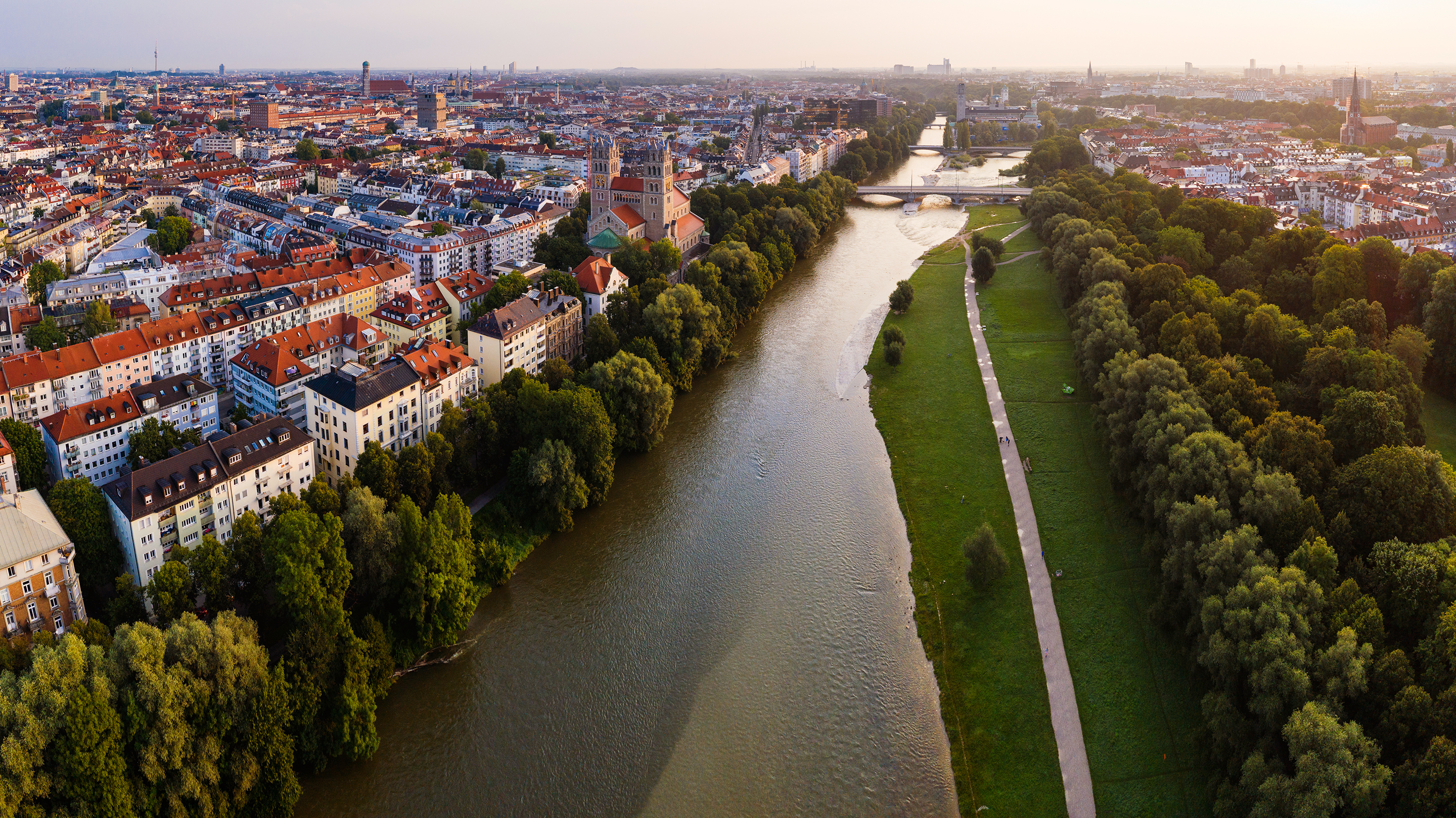Flyfoto av München med en elv, trær og en gangvei langs elven.