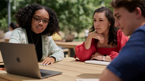 Dos estudiantes universitarias sentadas afuera de un campus de Apple.