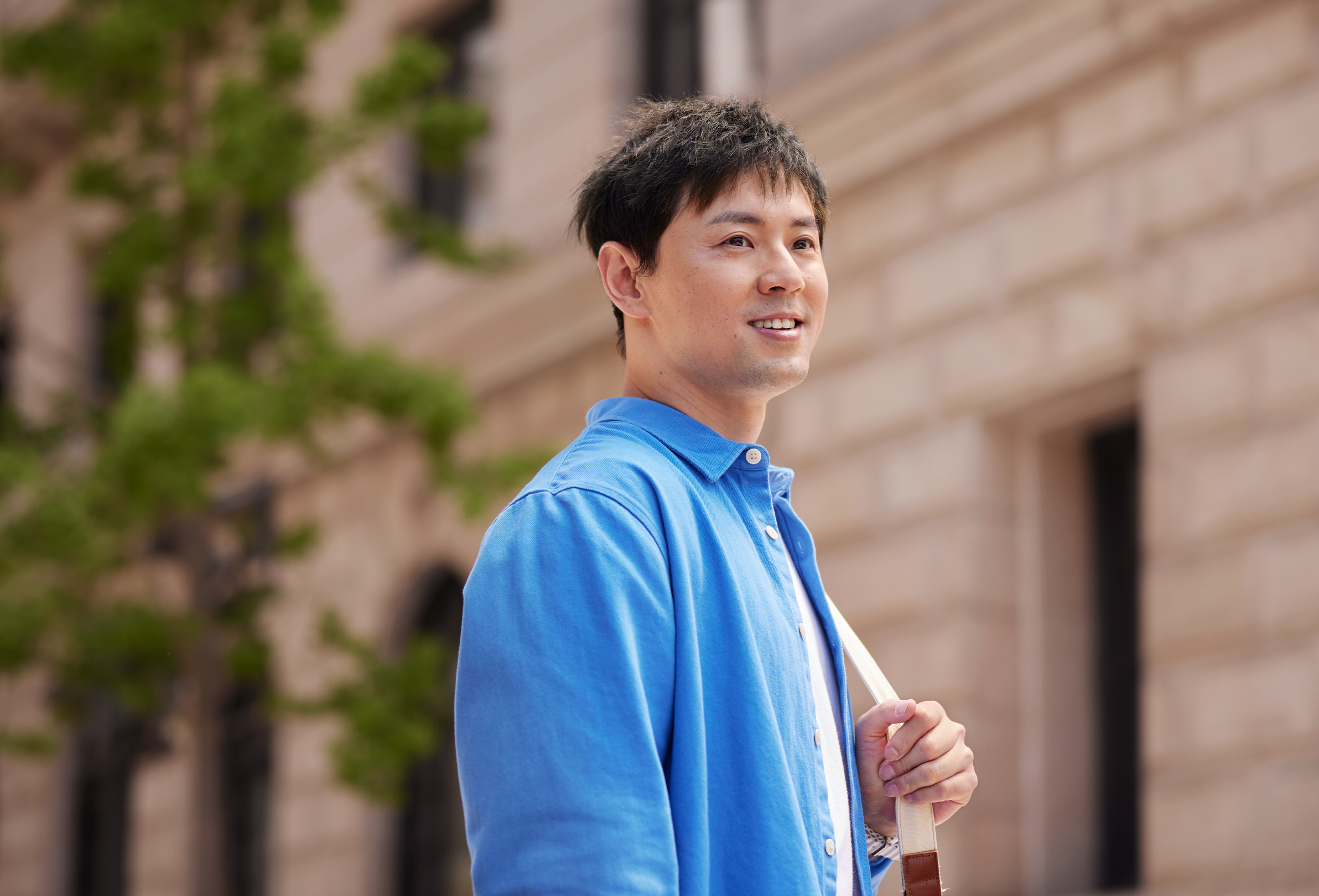 Een glimlachende Apple medewerker met een schoudertas staat buiten aan een stenen kantoorgebouw.