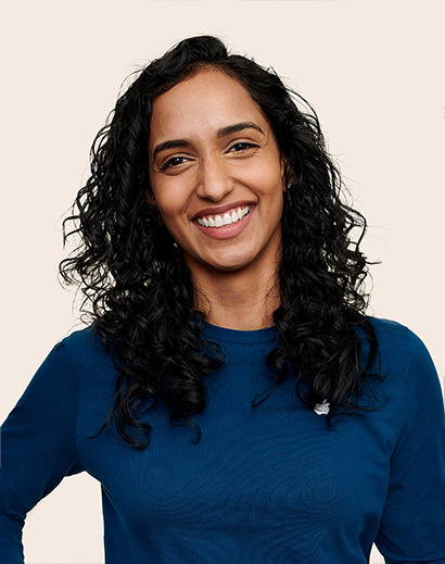 Apple Retail employee with shoulder-length curly hair, smiling at the camera.