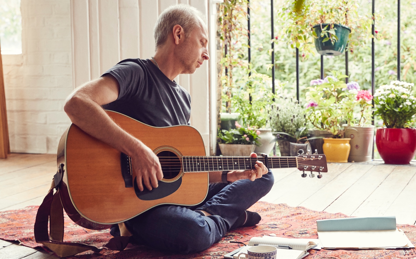 남성 Apple Store 직원이 집에서 바닥에 앉아 기타를 연주하는 모습