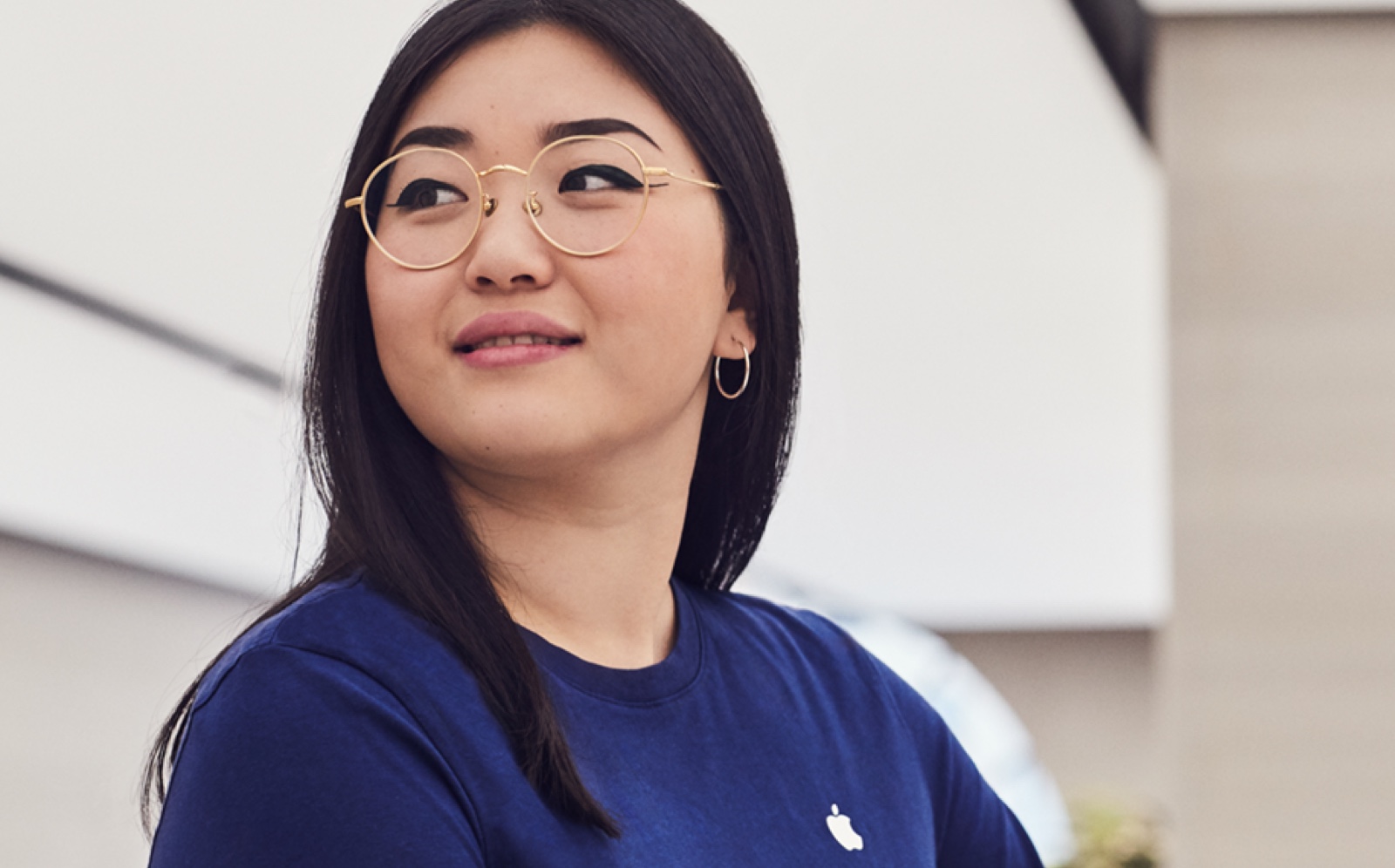 A female Apple Store employee stands in the store, smiling.