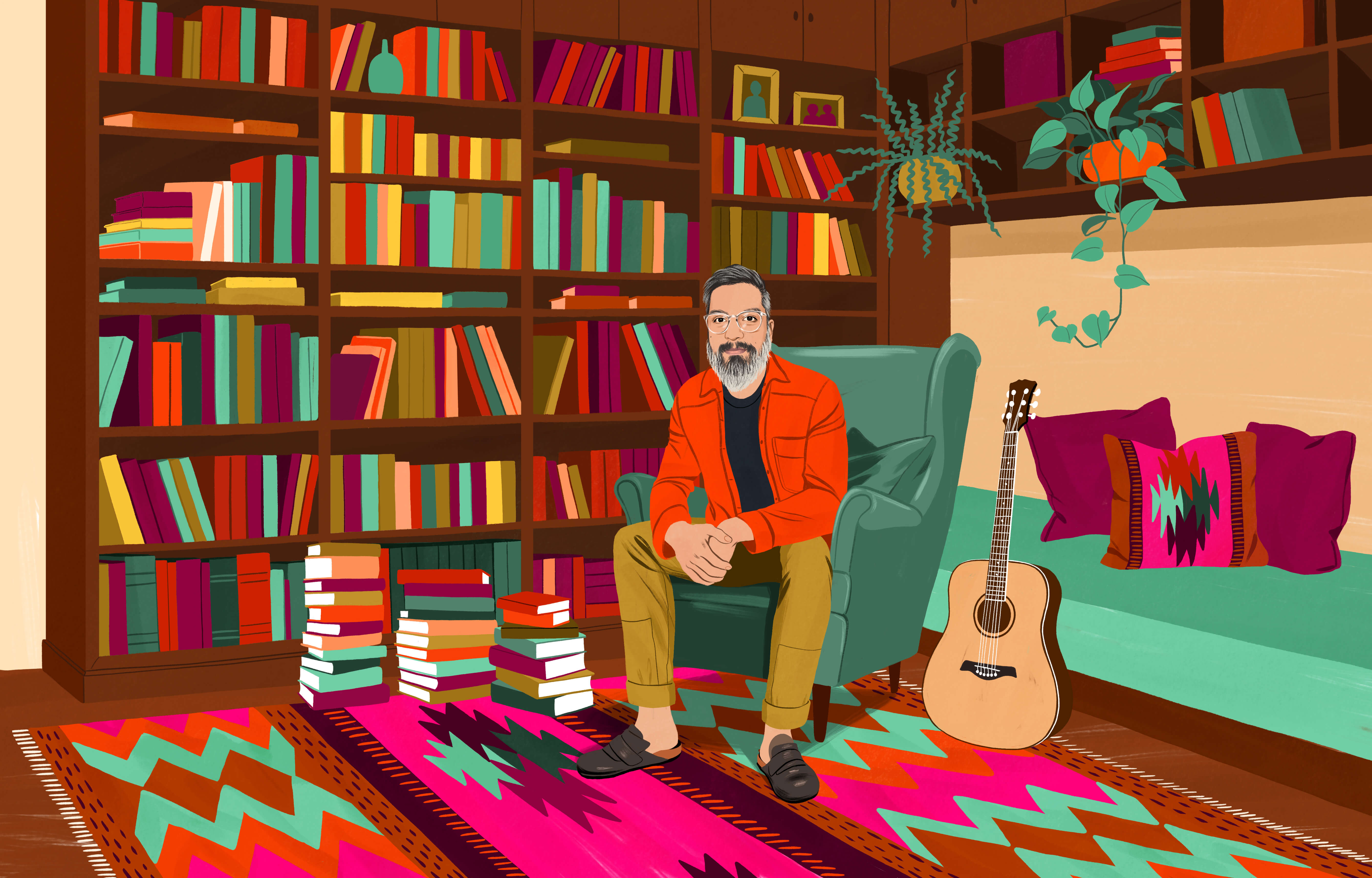 JP sitting in a wingback chair surrounded by many books in bookcases and stacked high on the floor. On the floor is a traditional Chilean rug with a colourful pattern. An acoustic guitar is within arm’s reach.