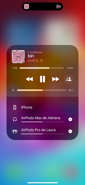 AirPods Pro en un estuche de carga junto a un iPhone, el iPhone está conectado a dos pares de AirPods, cada uno con su propio control de volumen.