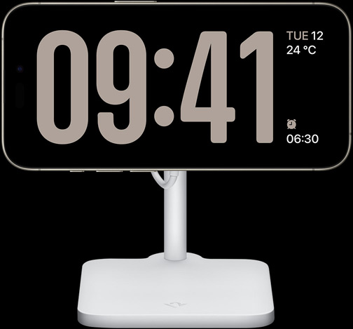 An iPhone 15 Pro in StandBy showing a full-screen clock along with the date, the temperature and the next alarm