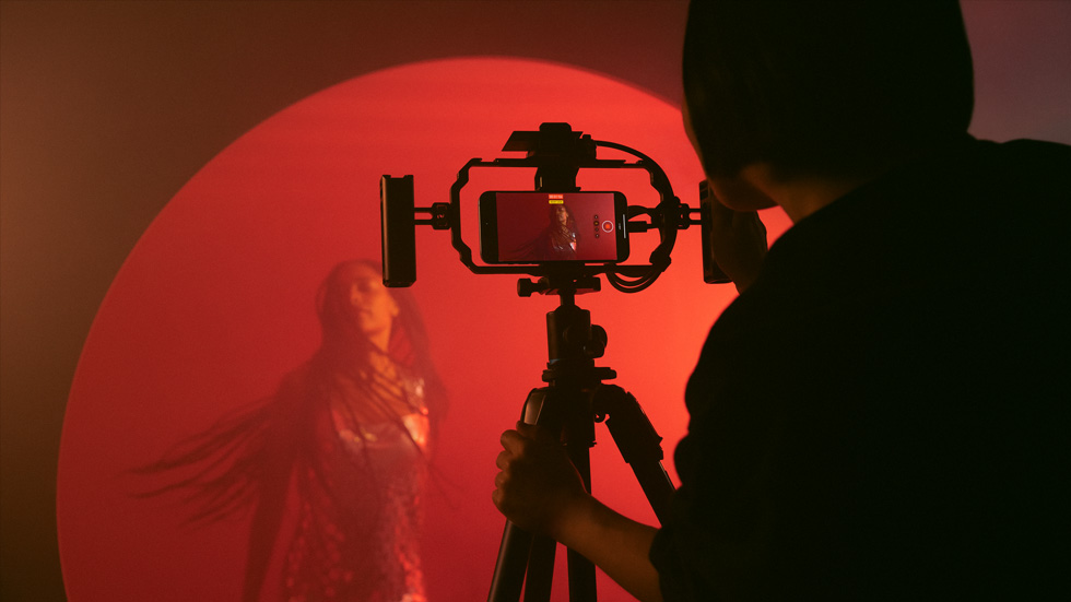 Poza unei persoane folosind un iPhone pe un trepied pentru a înregistra un videoclip plin de culoare cu o femeie