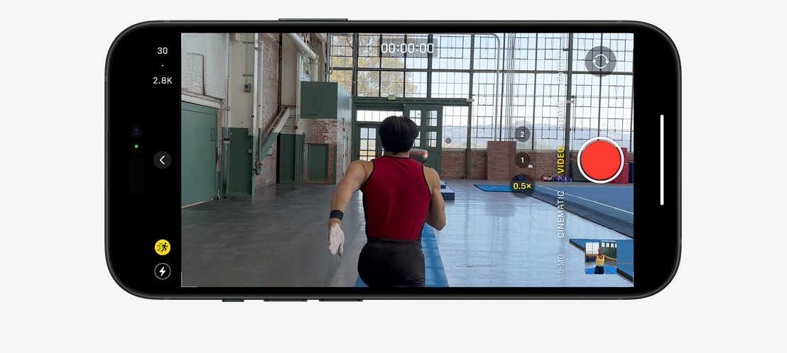 Vaizdas, kuriame „iPhone 15 Pro“ veiksmo režimu filmuojamas gimnastas, bėgantis didelėje, apšviestoje patalpoje.