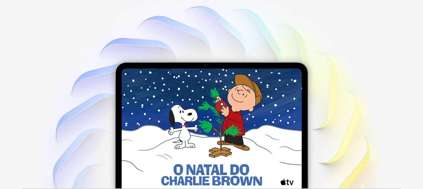 iPad Pro de 11 polegadas prateado, tela com a imagem do Charlie Brown decorando uma pequena árvore de Natal, o Snoopy olhando para a árvore, a neve caindo e o logotipo do Apple TV no canto inferior direito. Diversos quadrados angulares com bordas arredondadas nas cores azul, verde e amarela se desdobram por trás