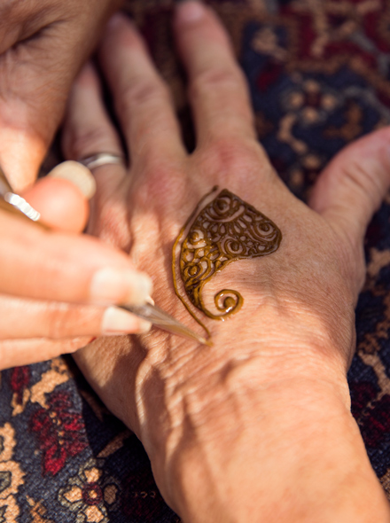 Un primo piano che mostra le mani di una persona che sta applicando un tatuaggio all’henné sulle mani di un’altra persona.