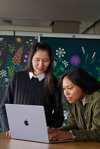 Zwei Mitglieder des Apple Marketing Teams arbeiten gemeinsam an einem MacBook vor Postern, die ihr Team designt hat.
