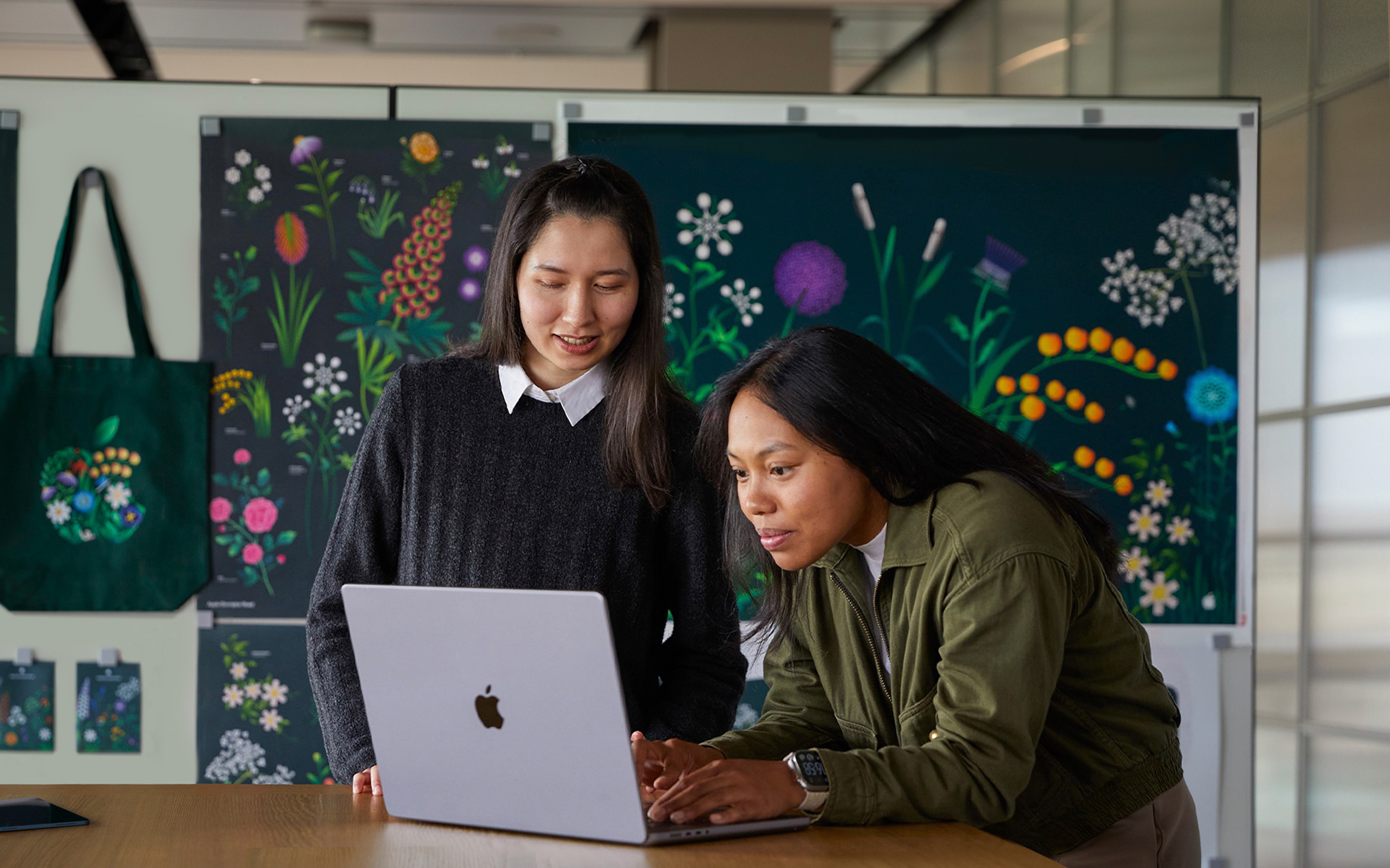 Due persone del team Marketing di Apple che collaborano su un MacBook di fronte a poster realizzati dal loro team.