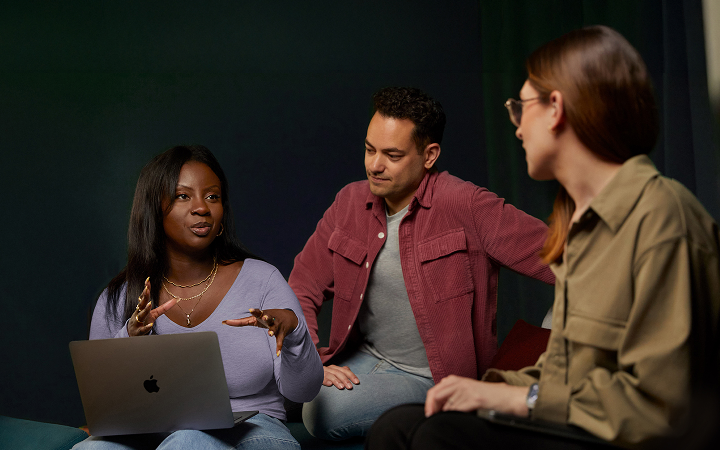 Drei Apple Software und Services Teammitglieder unterhalten sich auf einer Couch, eine Person mit einem MacBook.