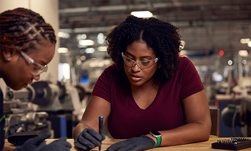 Camara e uma colega usam óculos de proteção enquanto trabalham juntas em um laboratório.