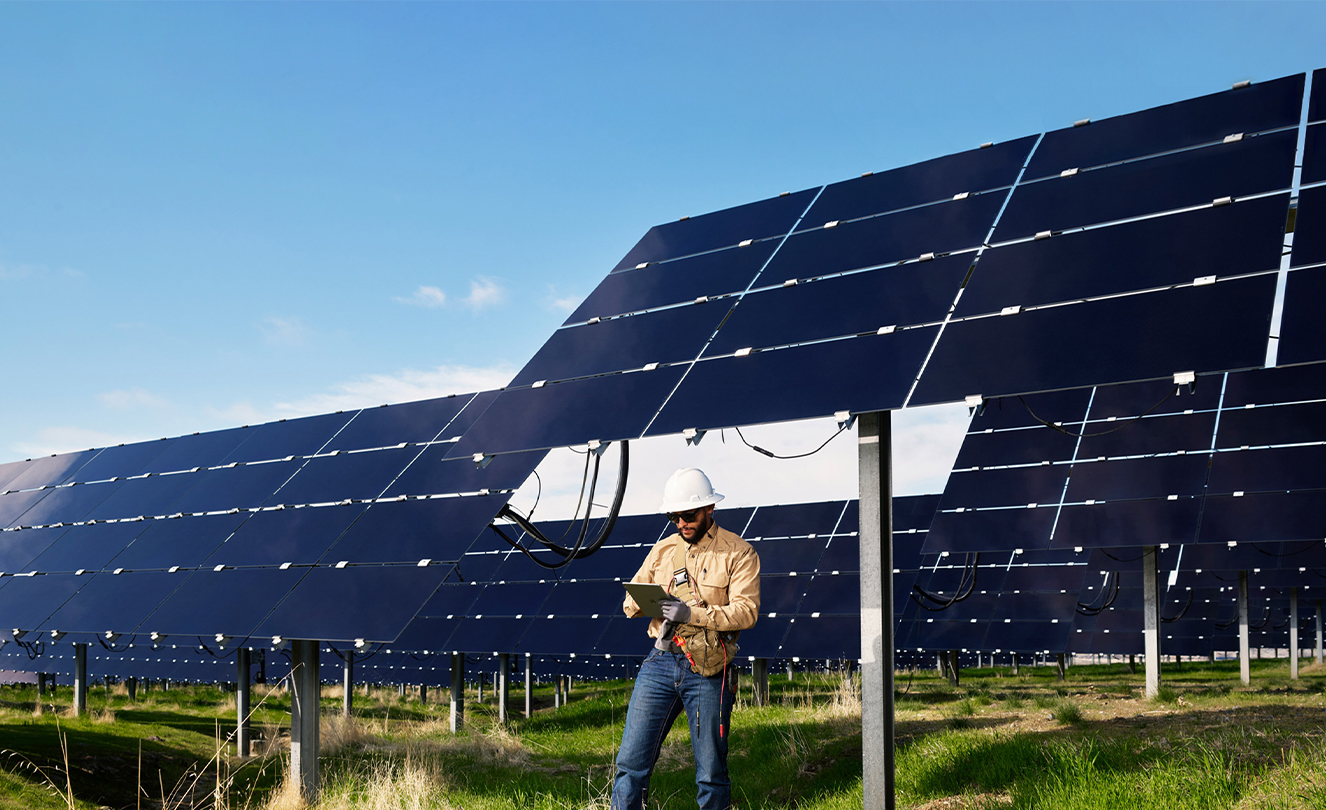 Man in hardhat working on his iPad standing on a field dotted with solar panels