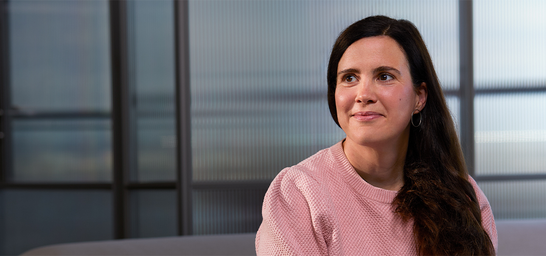 Lucie sitting indoors with a translucent glass wall behind her, smiling and looking to her right.