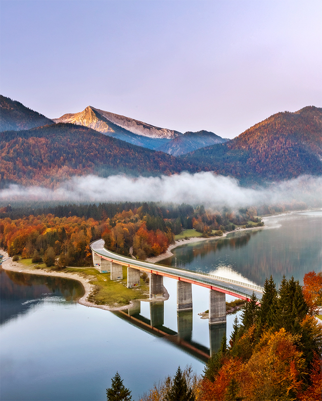 Uma ponte sobre um lago com montanhas ao fundo.