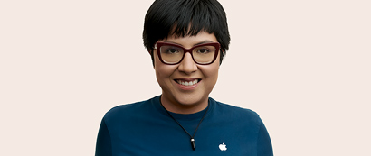 Kameraya doğru gülümseyen, kısa saçlı ve gözlüklü Apple Retail çalışanı.