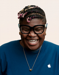 Apple Retail employee with a headscarf and glasses, smiling at the camera. 
