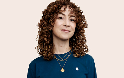 Apple Retail employee with curly hair, looking into the camera.