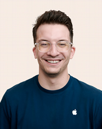 Kısa siyah saçlı, kameraya doğru gülümseyen Apple Retail çalışanı. 