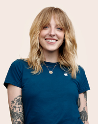 Membre de l’équipe Apple Retail avec des tatouages sur les bras, qui sourit à l’objectif.
