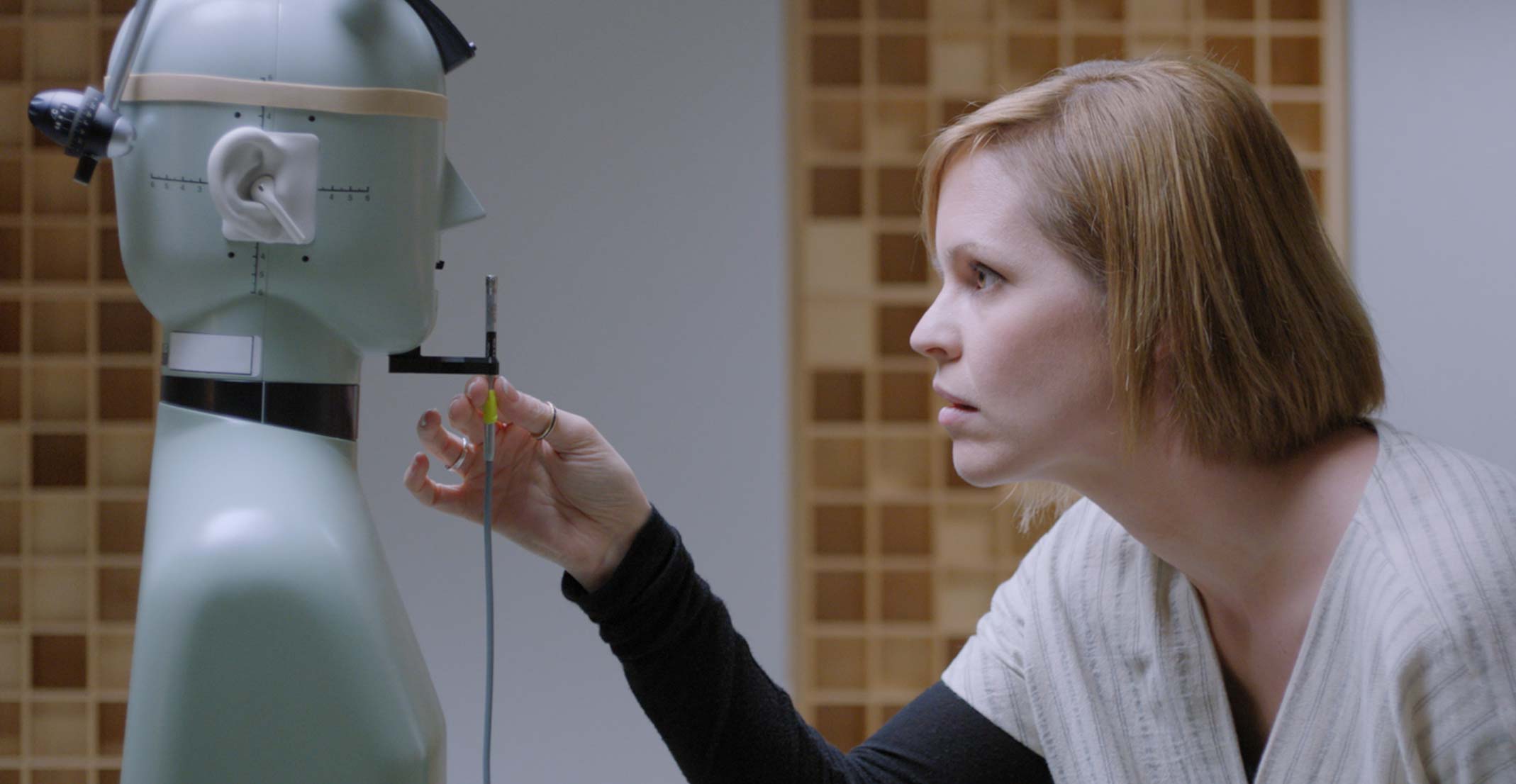 Suzie, manažerka týmu zabývajícího se akustickým prototypováním, upravuje mikrofon před figurínou v technické laboratoři v Cupertinu.