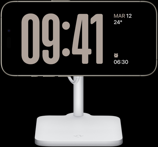 Un iPhone 15 Pro en modo En Espera muestra un reloj a pantalla completa con la fecha, la temperatura y la próxima alarma
