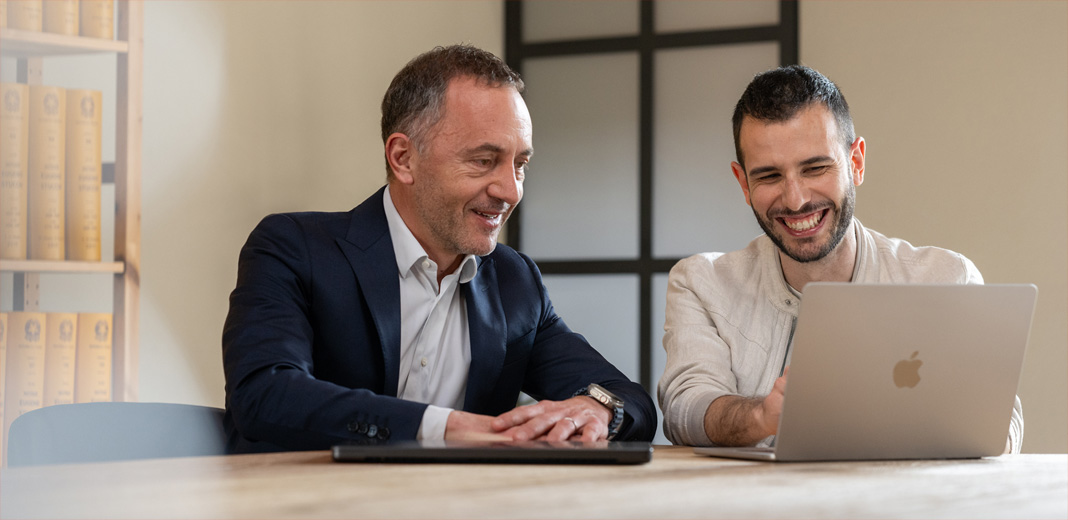 Due uomini che lavorano insieme davanti a un MacBook aperto.