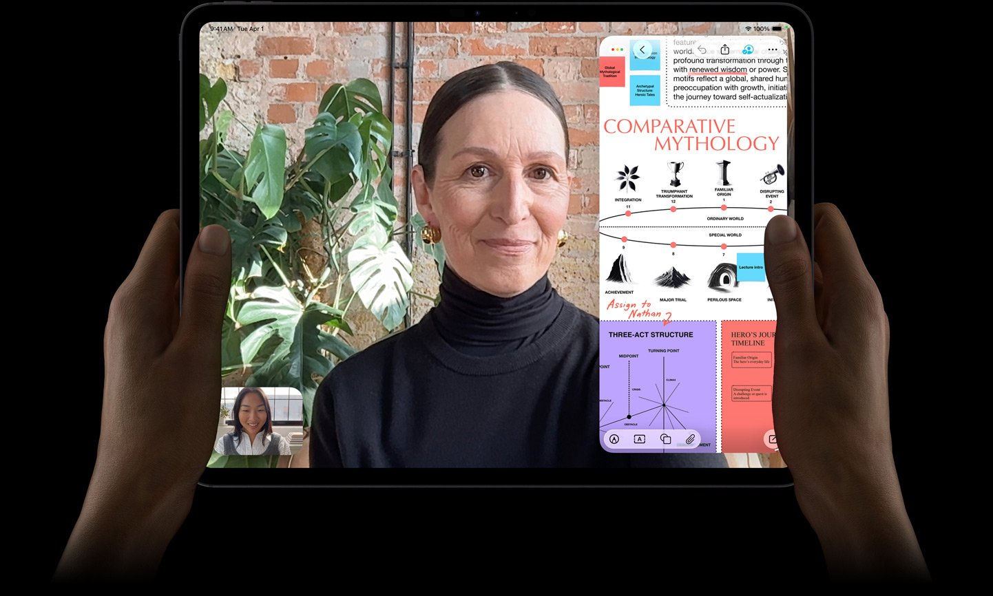 iPad Pro, front exterior, space black color, left and right hands holding in landscape orientation, rounded corners, black display bezel, display showing a FaceTime conversation being live translated, and an educational app showing a presentation of 'Comparative Mythology' with text, diagrams, and handwritten notes