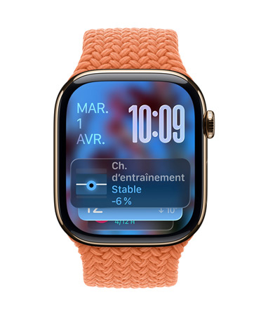 Une Apple Watch or rose avec un Bracelet tressé tangerine, le cadran affiche la date en haut à gauche, l’heure en chiffres superposés en haut à droite, le widget Charge d’entraînement en bas, le tout en Liquid Glass translucide