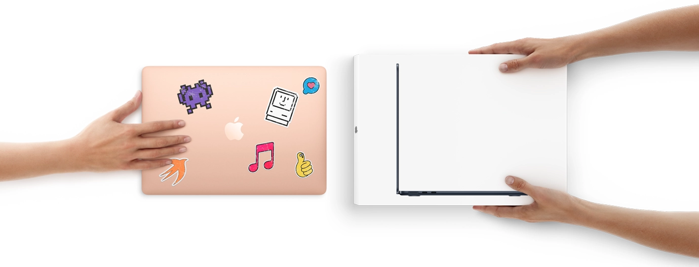 A hand slides a MacBook with stickers on the cover toward two hands holding a new MacBook in the box
