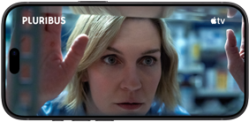 iPhone 18 Pro, pejzažni mod, prikazuje se krupni plan žene koja gleda kroz policu. Naslov serije: Pluribus