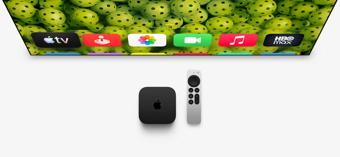Egy Apple TV 4K és az Apple TV Remote látható egy tévé alatt, amelyen a főképernyő tetején lévő appok ikonjai egy zöld pickleball-labdákat ábrázoló háttér előtt jelennek meg.
