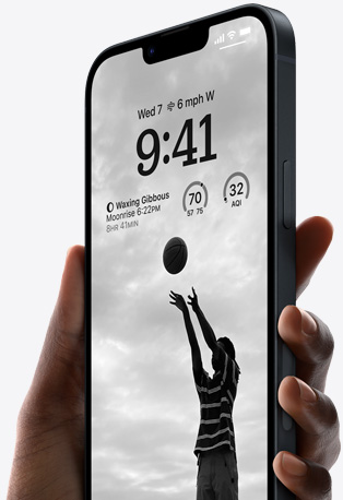 Tangan memegang iPhone 14 berwarna Midnight dengan Layar Terkunci yang dipersonalisasi serta memperlihatkan foto seseorang yang bermain basket, font hitam, dan widget