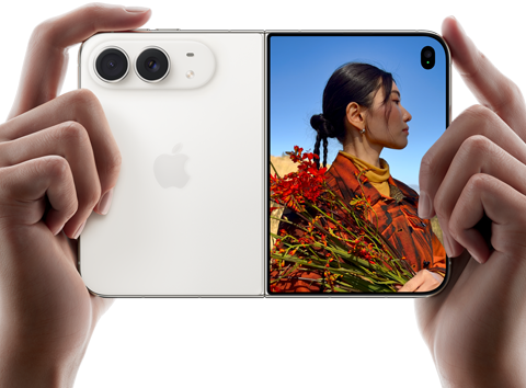 iPhone Duo, zvaigžņu baltā krāsā, tiek turēts divās rokās horizontālā novietojumā, atvērts, kreisajā panelī redzamas 48 MP Dual Fusion aizmugurējās kameras, labajā panelī redzams, kā ārējā displejā tiek uzņemta cilvēka bilde, fotografējamais redz savu seju, kamēr tiek uzņemta bilde ar Duo Preview