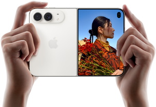 iPhone Duo, zvaigžņu baltā krāsā, tiek turēts rokās horizontālā novietojumā, atvērts, kreisajā panelī redzamas 48 MP Dual Fusion aizmugurējās kameras, labajā panelī redzams, kā ārējā displejā tiek uzņemta cilvēka bilde, fotografējamais redz savu seju, kamēr tiek uzņemta bilde ar Duo Preview
