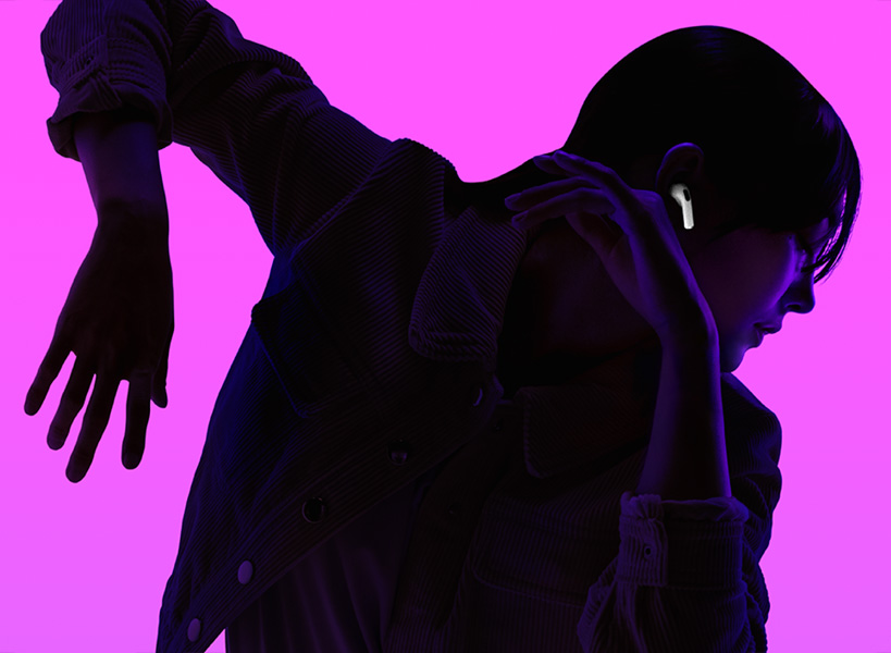 Silhouette of a person dancing with left arm angled down and right arm angled up, face is backlit in purple to highlight AirPods fitting securely in right ear.