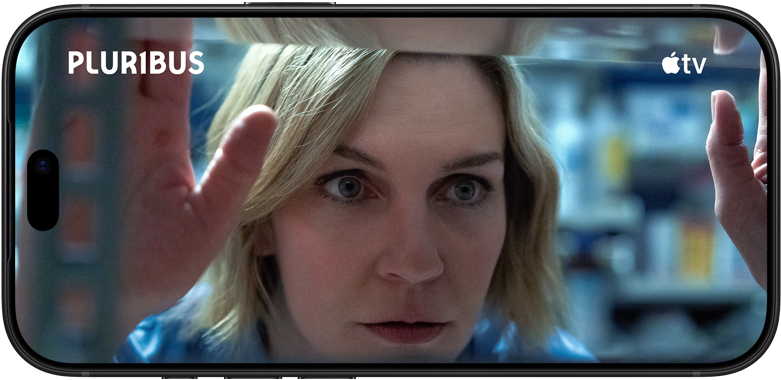 جهاز iPhone&nbsp;18&nbsp;Pro، الوضع الأفقي، يعرض لقطة مقرّبة لسيدة تنظر عبر النافذة. عنوان المسلسل: Pluribus‏