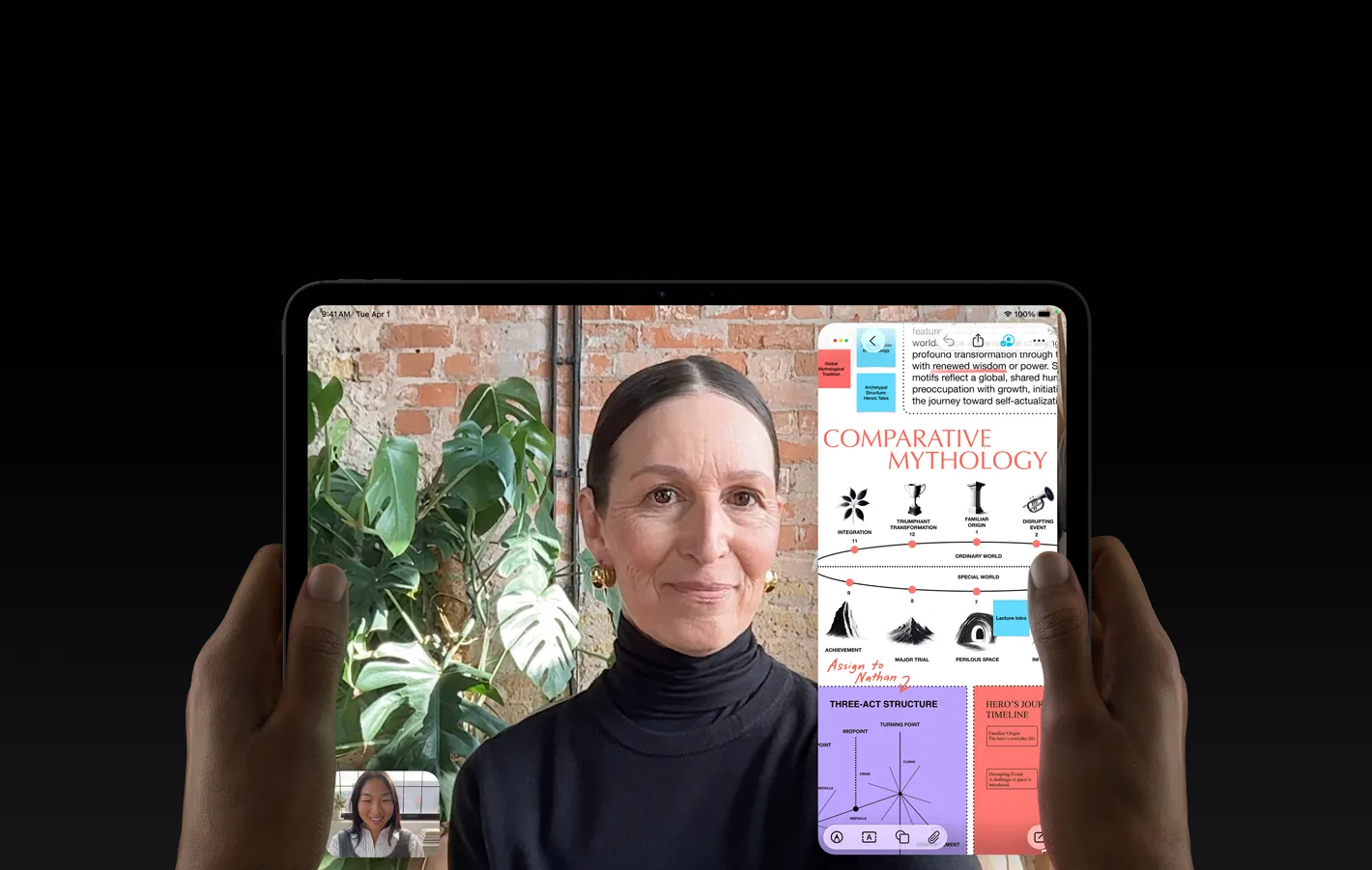 太空黑 iPad Pro 機身正面，左右手以橫向握持，展示圓角設計，黑色顯示器邊框，顯示器顯示正在實時翻譯一段 FaceTime 對話，以及一個教育 app 展示「Comparative Mythology」簡報，其中有文字、圖表和手寫筆記