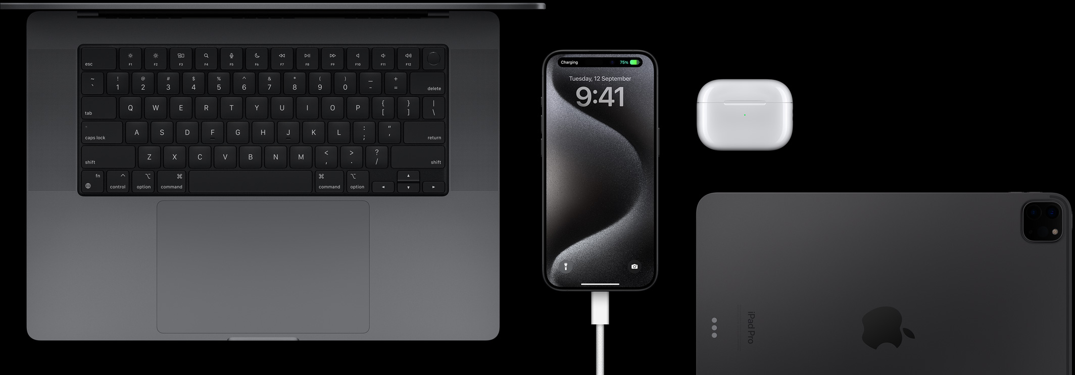 iPhone 15 Pro 插上 USB-C 連接線，周圍放著一部 MacBook Pro、一對 AirPods Pro 和一部 iPad