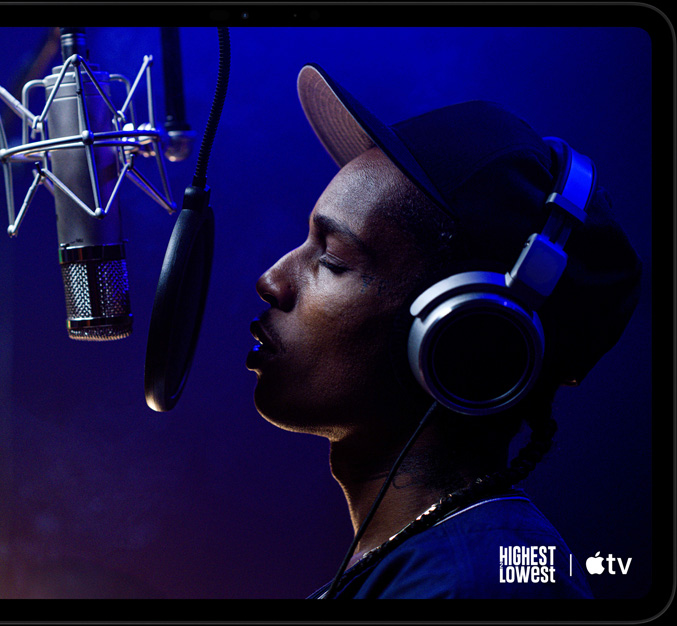 iPad Pro, landscape orientation, front exterior, space black colour, rounded corners, black display bezel, display showing Apple TV playing a scene from the Apple TV original film Highest 2 Lowest with ASAP Rocky as Yung Felon rapping into a microphone