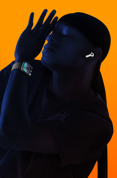 A person wearing AirPods and listening to music on an Apple Watch, with their eyes closed and leaning back with their hand raised towards their face.