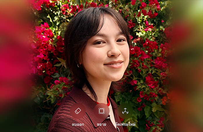 รูปภาพบุคคลที่มีผมสีน้ำตาลกำลังยิ้มแย้ม, สวมเสื้อสเวตเตอร์สีน้ำตาล, ล้อมรอบด้วยดอกไม้สีแดง, การสาธิตการปรับแต่งภาพถ่ายด้วย AI พร้อมตัวเลือกในการลบออก ขยาย และจัดเฟรมใหม่ที่แสดงอยู่เหนือภาพ