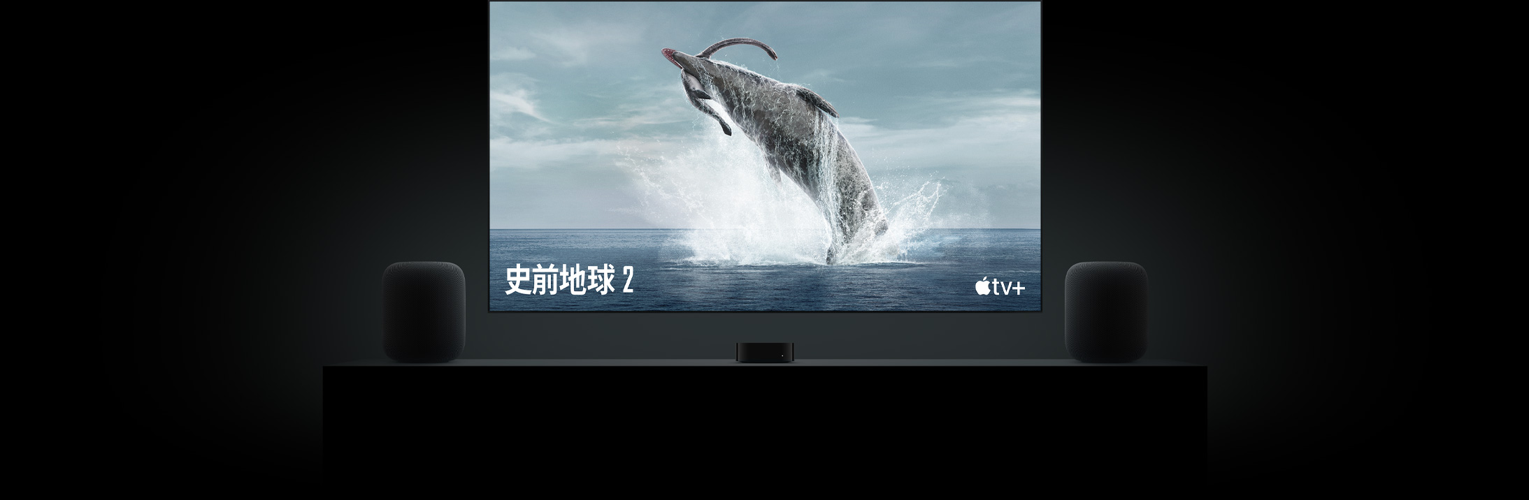 大型平面電視螢幕展示《史前地球》裡生動逼真的恐龍影像。電視懸掛在 Apple TV 上方，兩部 HomePod 揚聲器分別放在客廳電視櫃兩側