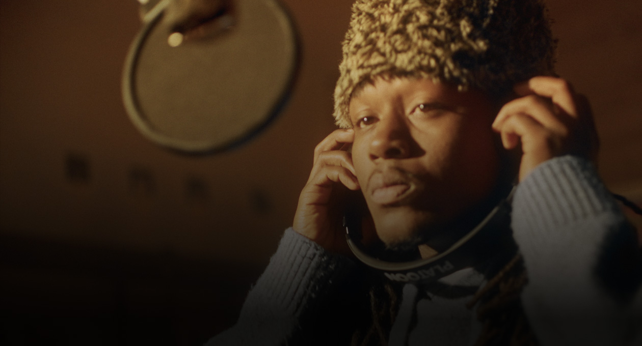 Foto de Kiddo K en un estudio de música frente a un micrófono de grabación y con audífonos puestos