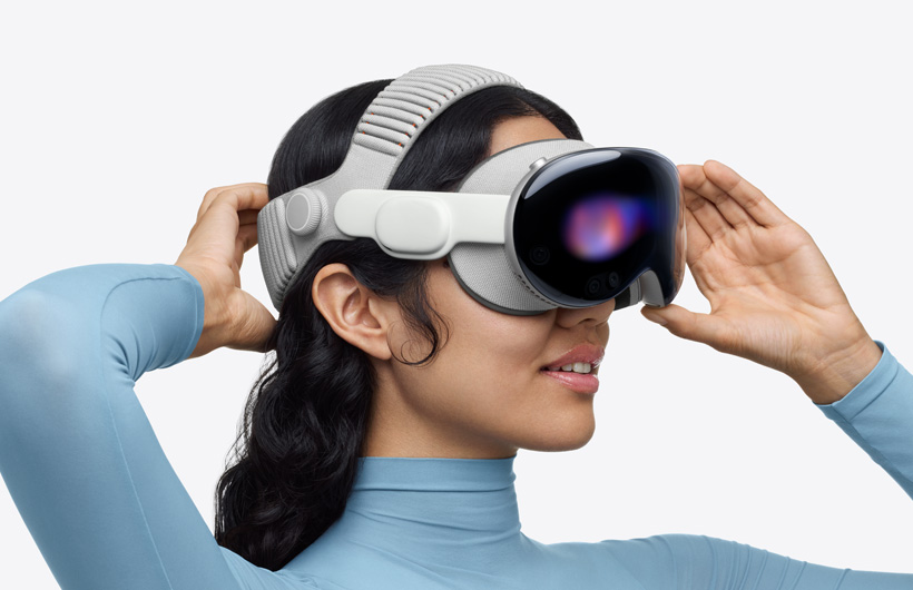 Person wearing Apple Vision Pro, assembled with Dual Knit Band, upper band spans across the top of the head, one hand placed on lower back band behind head, other hand placed on aluminium alloy frame