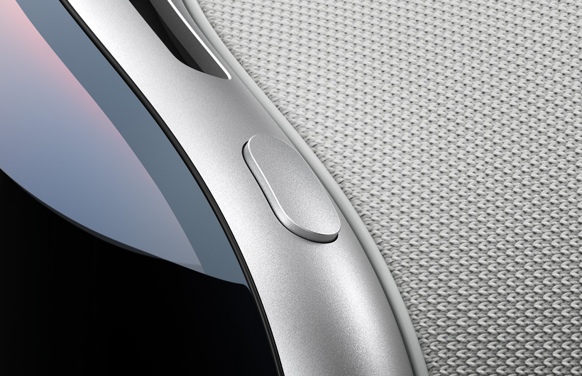 Close-up view shows the curved top-left corner of Apple Vision Pro, the top button has the same aluminium finish as the Apple Vision Pro frame, the curved glass of the front and part of the top air vent are also shown