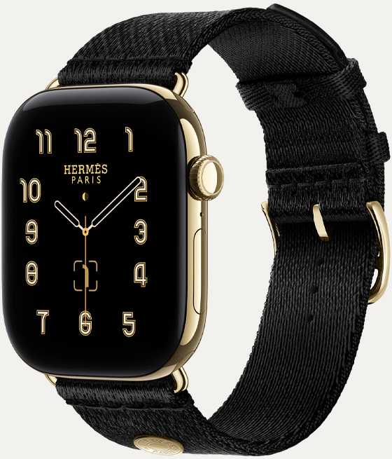 Apple Watch Hermès Series 12, cadran analogique Clou de Selle (aiguilles des heures, des minutes et des secondes, complications : calendrier lunaire, date), boîtier en titane, or brillant, côté droit, Digital Crown, bouton latéral, associée au bracelet Clou de Selle Satin Noir, tissu satiné noir avec attaches or brillant assorties au boîtier de la montre